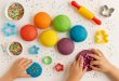 Rainbow edible play dough balls with sprinkles and cookie cutters on a white tabl
