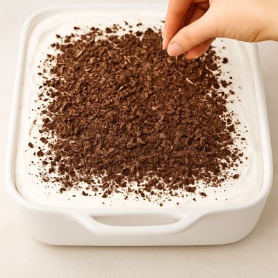 Topping with Cool Whip and chocolate shavings before chilling No-Bake Chocolate Cherry Lush: Layered Dessert Recipe