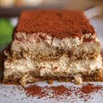 Delicious tiramisu dessert with creamy layers and a dusting of cocoa powder on a white plate and ladyfingers