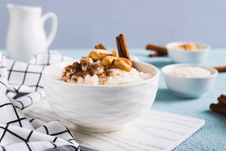 Close-up of a single white bowl filled with rich arroz con leche, sprinkled with cinnamon and cashews, set against a blue backdrop for a classic Mexican treat.and condensed milk