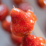 Close-up of glossy Tanghulu, a popular asian.candy, featuring fresh strawberries coated in a crispy sugar shell, making it a delicious candied fruit treat.