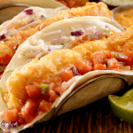 Close-up de un fish taco crujiente con rebozado dorado, cubierto con coleslaw y pico de gallo. Inspirado en ideas del del taco menu y fusionado con técnicas de birria tacos recipe, perfecto para disfrutar en taco time y fácilmente adaptable con tilapia recipes