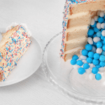 gender-reveal-cakeA slice of cake on a plate next to a layered reveal cake spilling blue candies, highlighting the excitement of the moment.