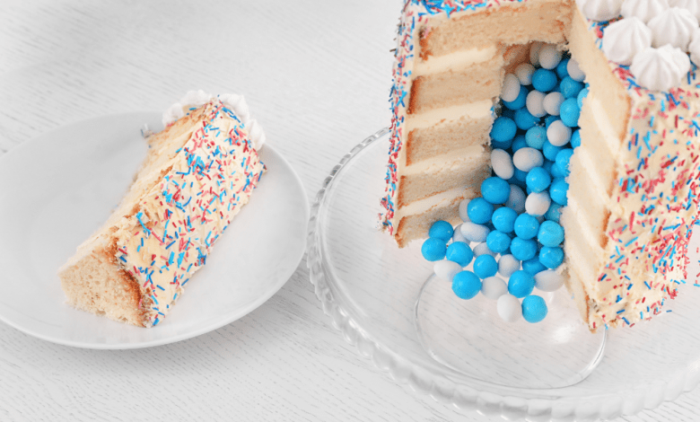 "Oh Sweet Surprise: Baby Gender Reveal Cake by Your Favorite Bakery" 11 gender-reveal-cakeA slice of cake on a plate next to a layered reveal cake spilling blue candies, highlighting the excitement of the moment.