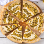 Pickle Pie Pizza Sliced dill pickle pizza on a wooden board with a golden crust and creamy garlic drizzle.
