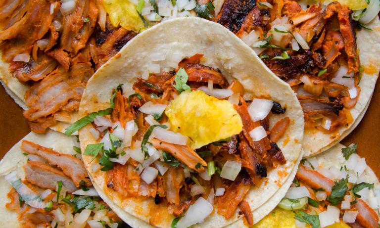 Close-up of tacos al pastor with juicy marinated pork, fresh cilantro, and a slice of pineapple.