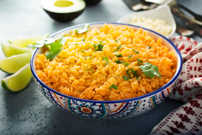 Spanish Rice recipe A ceramic bowl of orange-hued Spanish rice decorated with fresh cilantro leaves, accompanied by lime wedges for a zesty touch.