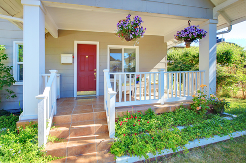 Grey house porch with red door and white railings.