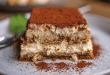 Delicious tiramisu dessert with creamy layers and a dusting of cocoa powder on a white plate and ladyfingers