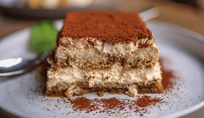 Delicious tiramisu dessert with creamy layers and a dusting of cocoa powder on a white plate and ladyfingers