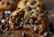 Chocolate Chip Cookie Recipe Close-up of a freshly baked chocolate chip cookie with melted chocolate chips, placed on a rustic wooden table.