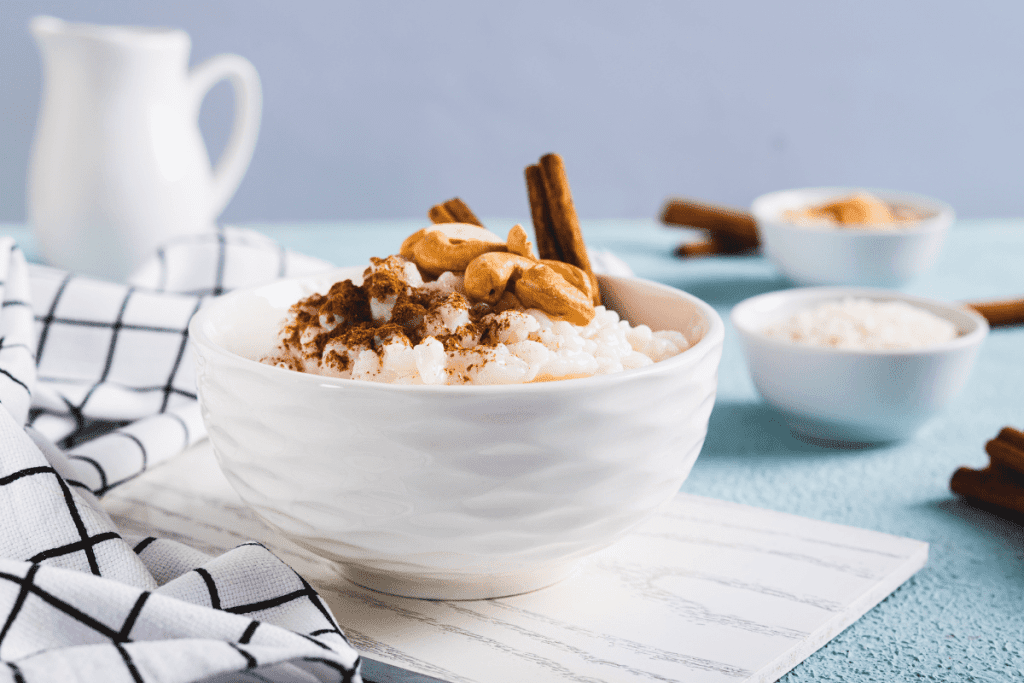 The Best Arroz con Leche Mexicano | Enjoy Authentic Mexican Rice Pudding {Muy Delicioso!} 11 Close-up of a single white bowl filled with rich arroz con leche, sprinkled with cinnamon and cashews, set against a blue backdrop for a classic Mexican treat.and condensed milk