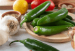 Fresh serrano peppers on a wooden plate surrounded by ingredients like garlic, lemon, and tomatoes, ready for cooking
