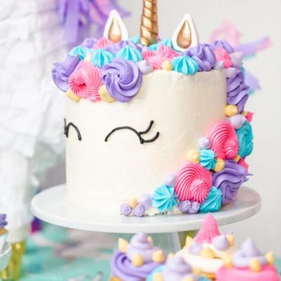 Finished unicorn cake with colorful frosting decorations, a golden horn, and eyes drawn on the icing.