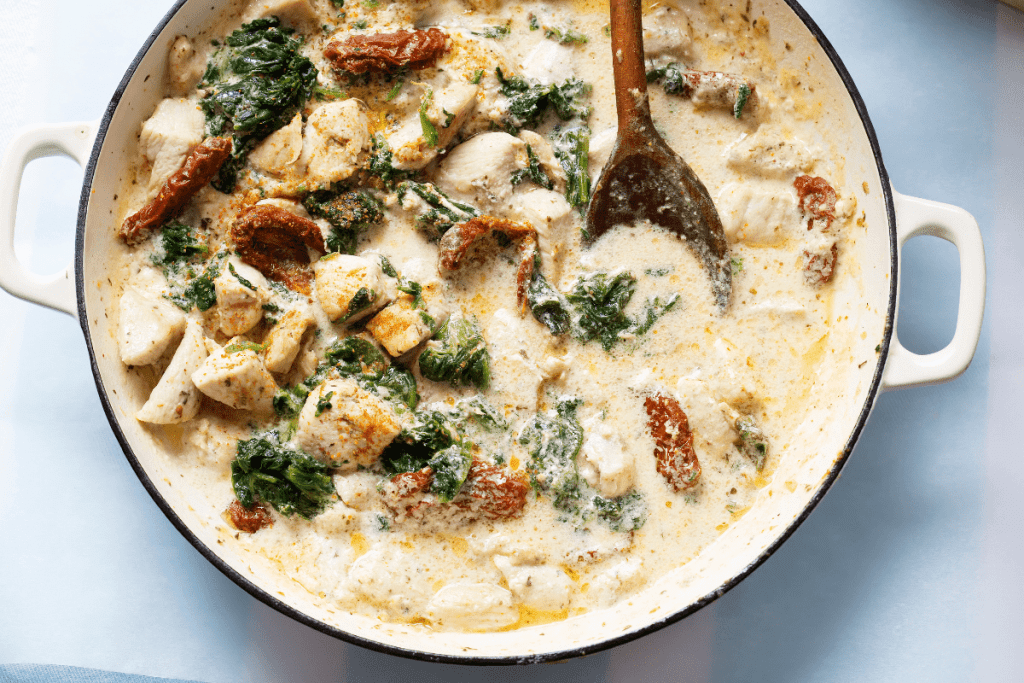 A bright, close-up image featuring tender chicken chunks nestled in a creamy, garlic-infused sauce. The spinach and sun-dried tomatoes add pops of color, illustrating the dish’s indulgent texture and hearty appeal.