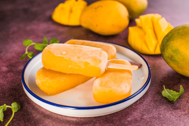 A close-up of vibrant yellow mango-flavored Mexican popsicles, or paletas, from La Michoacana, served on a plate with fresh mango slices and mint leaves, against a rustic background. yogurt