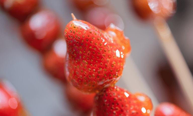 Close-up of glossy Tanghulu, a popular asian.candy, featuring fresh strawberries coated in a crispy sugar shell, making it a delicious candied fruit treat.