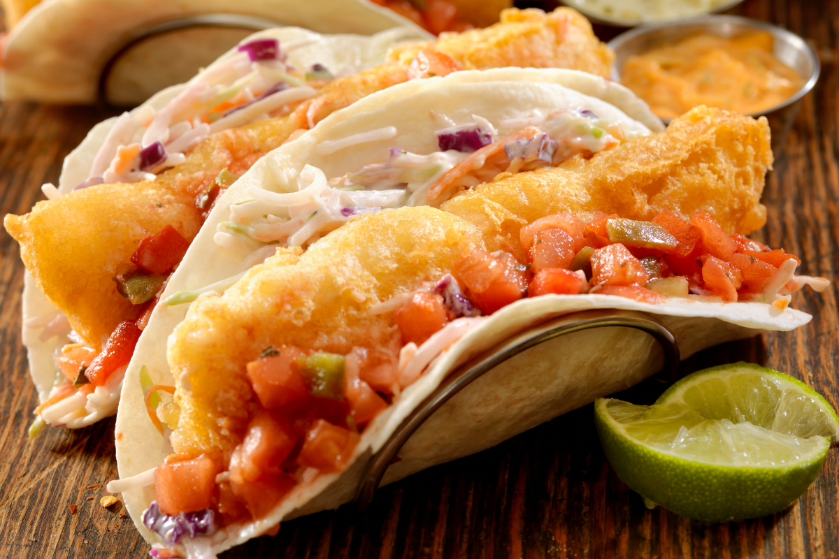Close-up de un fish taco crujiente con rebozado dorado, cubierto con coleslaw y pico de gallo. Inspirado en ideas del del taco menu y fusionado con técnicas de birria tacos recipe, perfecto para disfrutar en taco time y fácilmente adaptable con tilapia recipes