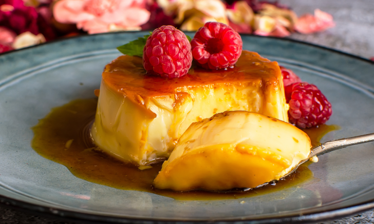 A silky slice of flan topped with fresh raspberries and caramel sauce, revealing its soft, custardy center make with condensed milk