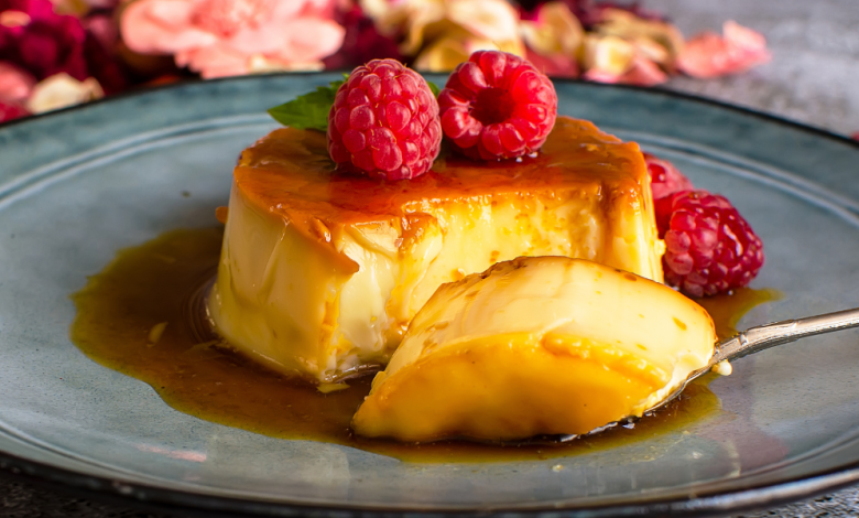 A silky slice of flan topped with fresh raspberries and caramel sauce, revealing its soft, custardy center make with condensed milk