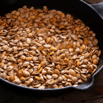A close-up of freshly roasted pepitas in a cast-iron pan, capturing their crunchy, seasoned surface and inviting color—ideal for garnishing salads, soups, or simply enjoying as a nutritious snack.