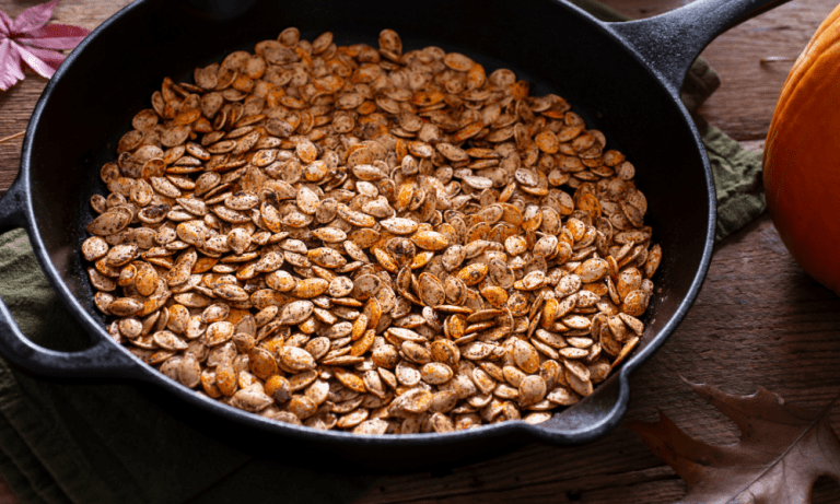 A close-up of freshly roasted pepitas in a cast-iron pan, capturing their crunchy, seasoned surface and inviting color—ideal for garnishing salads, soups, or simply enjoying as a nutritious snack.