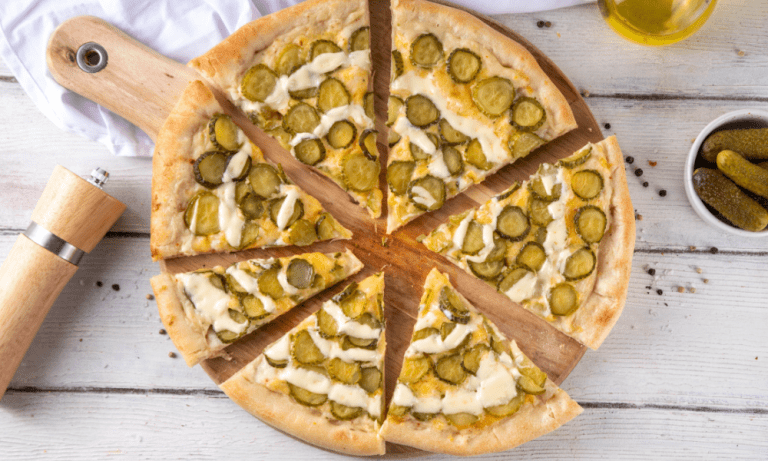 Pickle Pie Pizza Sliced dill pickle pizza on a wooden board with a golden crust and creamy garlic drizzle.