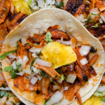 Close-up of tacos al pastor with juicy marinated pork, fresh cilantro, and a slice of pineapple.