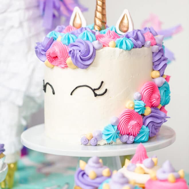 Finished unicorn cake with colorful frosting decorations, a golden horn, and eyes drawn on the icing.