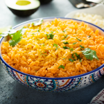 Spanish Rice recipe A ceramic bowl of orange-hued Spanish rice decorated with fresh cilantro leaves, accompanied by lime wedges for a zesty touch.