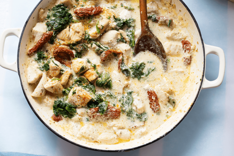 A bright, close-up image featuring tender chicken chunks nestled in a creamy, garlic-infused sauce. The spinach and sun-dried tomatoes add pops of color, illustrating the dish’s indulgent texture and hearty appeal.
