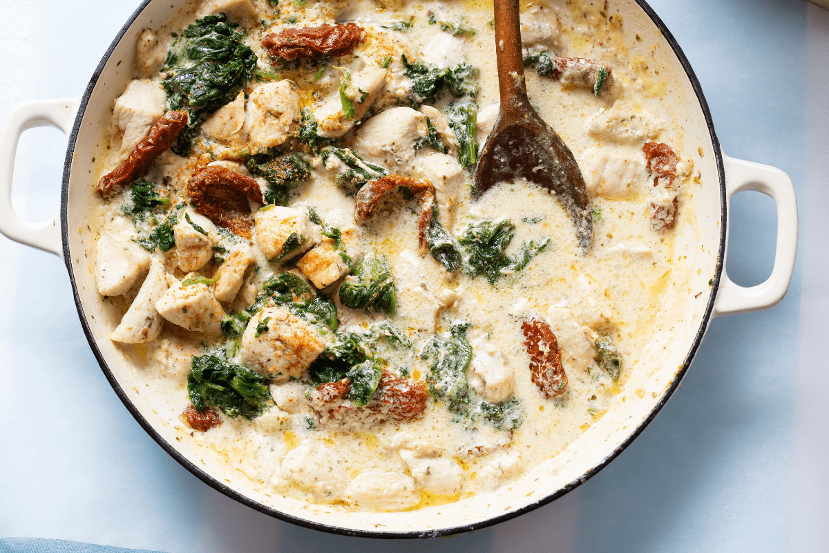 A bright, close-up image featuring tender chicken chunks nestled in a creamy, garlic-infused sauce. The spinach and sun-dried tomatoes add pops of color, illustrating the dish’s indulgent texture and hearty appeal.